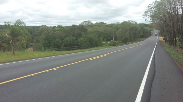A foto destaca um longo trecho da ERS-467, com asfalto e pintura recém renovados. Céu parcialmente nuclado e vegetação às margens da rodovia compõem o cenário.