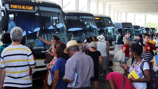 A foto mostra um grande número de passageiros aguardando o embarque dos ônibus na rodoviária de Porto Alegre. Os veículos estão todos estacionados.