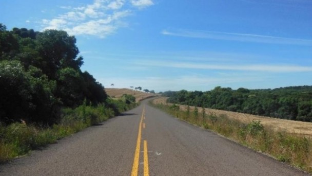 A foto mostra um longo trecho pavimentado e sinalizado da ERS-462, em Muliterno. O asfalto está com o eixo central pintado e a rodovia possui, às margens, campo e árvores. O céu azul com poucas nuvens completa a paisagem.