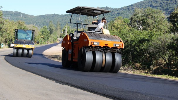 A foto mostra duas máquinas com rolo compressor atuando nas obras de restauração de uma rodovia