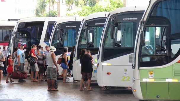 A foto mostra diversos ônibus estacionados no setor de embarque da Rodoviária de Porto Alegre, com passageiros fazendo fila para entrar nos mesmos.