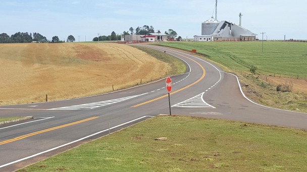 A foto mostra uma interseção na RSC-377, na Região Central do Rio Grande do Sul. O asfalto está restaurado, com sinalização. Ao fundo, a paisagem é formada por lavouras e um silo de grãos.