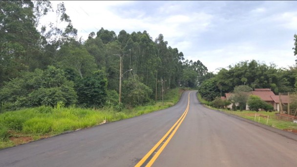 A foto mostra um trecho pavimentado da VRS-874, em São José do Hortêncio, no Vale do Caí. Além do asfalto, a estrada está com a faixa do eixo central pintada em amarelo. Ao fundo, árvores e casas do interior.
