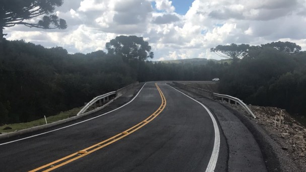 A foto mostra a rodovia ERS-332. Na lateral da estrada, árvores. A pista está sinalizada e defensas metálicas implantadas nas bordas da estrada.