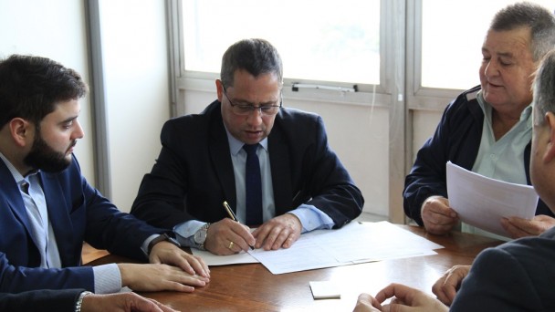 A foto mostra o diretor-geral do Daer, Rogério Uberti, com uma caneta na mão assinando a ordem de início de Caraá. Ao lado dele, demais autoridades acompanham a assinatura.