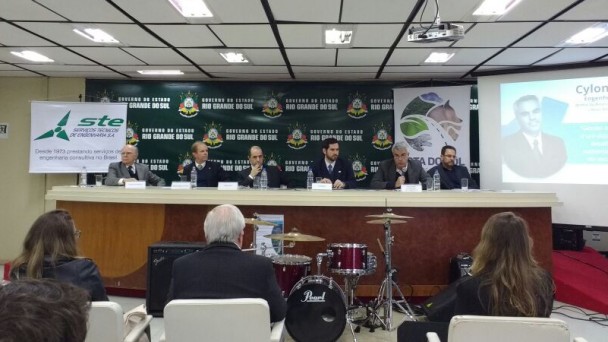 A foto mostra uma mesa com os cinco debatedores do painel sobre o desafio da gestão ambiental de rodovias e o mediador, jornalista André Machado. Em primeiro plano, o público no auditório do CAFF, de costas para a câmera, assistindo ao debate.