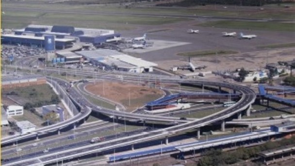 Foto área mostrando viadutos e alças de acesso ao Aeroporto Internacional Salgado Filho, em Porto Alegre. Ao fundo, as instalações do aeroporto e alguns aviões estacionados.