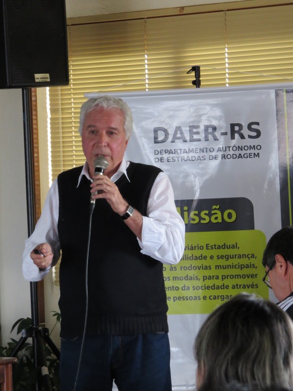 Engenheiro grisalho, com banner do Daer ao fundo, fala ao microfone durante palestra