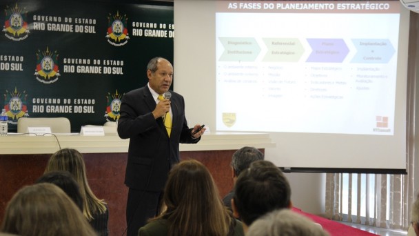 Na foto, o consultor Alfredo Guimarães fala ao microfone, com o público à frente. Atrás dele, um projetor apresenta um slide intitulado As Fases do Planejamento Estratégico.