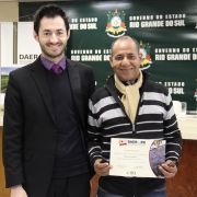 A imagem mostra um servidor do Daer recebendo de um diretor um certificado de homenagem pelos serviços prestados à autarquia.