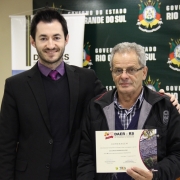 A imagem mostra um servidor do Daer recebendo de um diretor um certificado de homenagem pelos serviços prestados à autarquia.