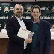 A imagem mostra um servidor do Daer recebendo de um diretor um certificado de homenagem pelos serviços prestados à autarquia.