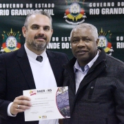 A imagem mostra um servidor do Daer recebendo de um diretor um certificado de homenagem pelos serviços prestados à autarquia.