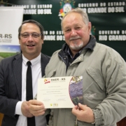 A imagem mostra um servidor do Daer recebendo de um diretor um certificado de homenagem pelos serviços prestados à autarquia.