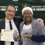 A imagem mostra um servidor do Daer recebendo de um diretor um certificado de homenagem pelos serviços prestados à autarquia.