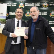A imagem mostra um servidor do Daer recebendo de um diretor um certificado de homenagem pelos serviços prestados à autarquia.