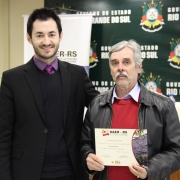 A imagem mostra um servidor do Daer recebendo de um diretor um certificado de homenagem pelos serviços prestados à autarquia.