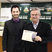 A imagem mostra um servidor do Daer recebendo de um diretor um certificado de homenagem pelos serviços prestados à autarquia.