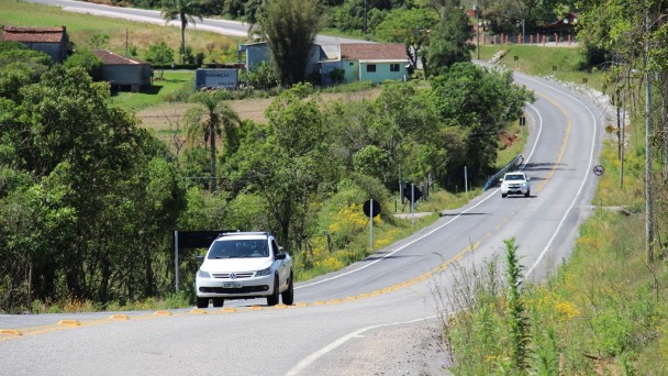 A foto mostra o recém inaugurado acesso municipal a Arroio do Padre. A estrada está com asfalto novo, placas e tachões. Dois veículos transitam pela via.