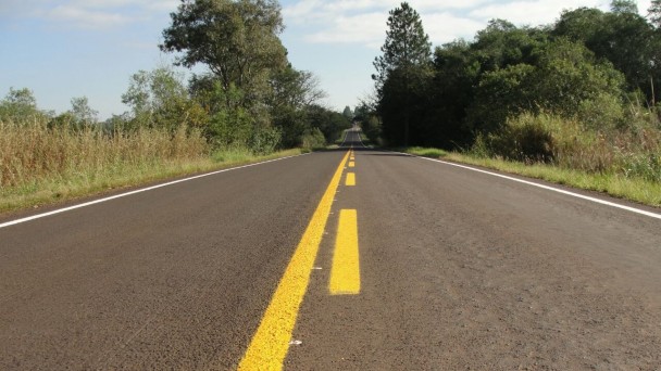 A foto mostra um trecho longo da rodovia ERS-540, com destaque para a faixa amarela do eixo central recém pintada. Às margens, vegetação.