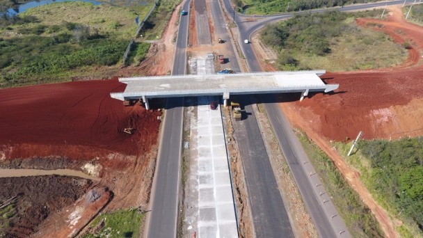 A foto mostra uma visão aérea das obras de duplicação da ERS-118, com destaque para a construção dos acessos de um viaduto sobre a rodovia, ainda terraplanados.