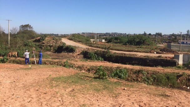 A foto mostra o terreno onde será construída a ponte sobre o Arroio Pampa, na Avenida dos Municípios, em Novo Hamburgo. Dois funcionários da construtora fazem levantamento topográfico no trecho.