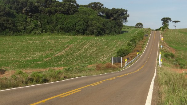 A imagem mostra um longo trecho da ERS-428, no acesso ao município de Água Santa, no Norte do Rio Grande do Sul. A estrada é asfaltada, sinalizada e possui às margens lavouras e árvores