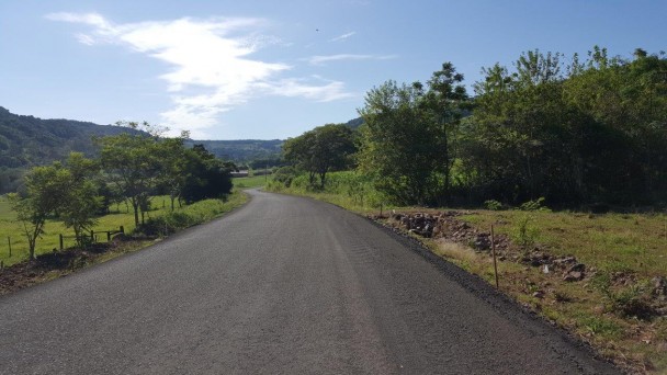 A foto mostra uma rodovia com pista sem imperfeições. O asfalto ainda não está sinalizado. Nas margens, vegetação.