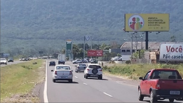 A foto mostra uma rodovia com pista dupla. Na margem direita, está um outdoor com a mensagem: "Empatia no trânsito. Você no lugar dos outros."