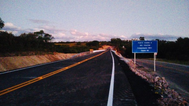 A foto mostra a Ponte do Costa. Ao lado, uma placa indicando que ela possui 160 m de comprimento e restrição a 45 toneladas