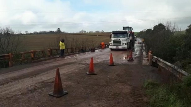 a foto mostra um caminhão atravessando a ponte da RSC-377. Ao lado, cones indicam que a obra ainda está em andamento.