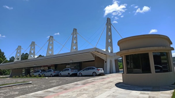 Na imagem aparece a rodoviária. No estacionamento dela estão carros estacionados. 