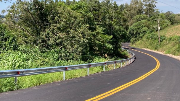 A foto mostra uma curva acentuada da rodovia. Ao redor, vegetação. 