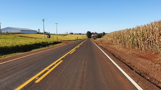 Foto mostra rodovia recém pavimentada e plantações no encostamento.