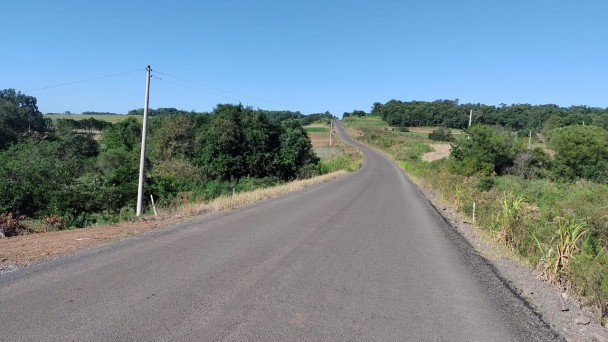 Na foto está a estrada do acesso a Ubiretama. Dos dois lados da imagem, há uma ampla vegetação, com uma mistura de árvores e gramado.