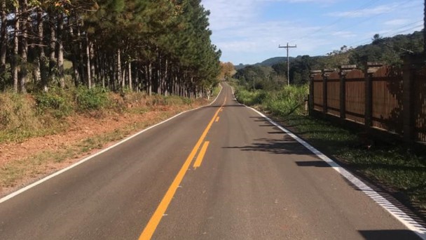 Na foto está a VRS-851 pavimentada com a grande presença de árvores dos dois lados. Está de dia e o céu está com bastante nuvens. 