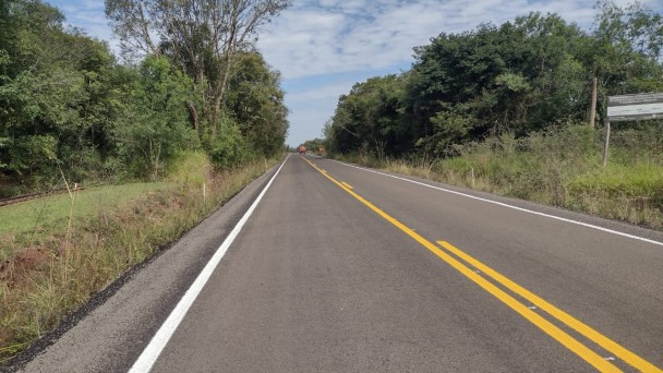 Na foto está a ERS-165 pavimentada. Dos dois lados de imagem chama a atenção a extensa vegetação, com várias árvores. A imagem é no dia e o céu está repleto de nuvens.