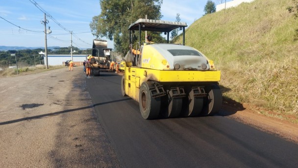 A foto mostra uma máquina com um rolo compressor passando por cima da rodovia.