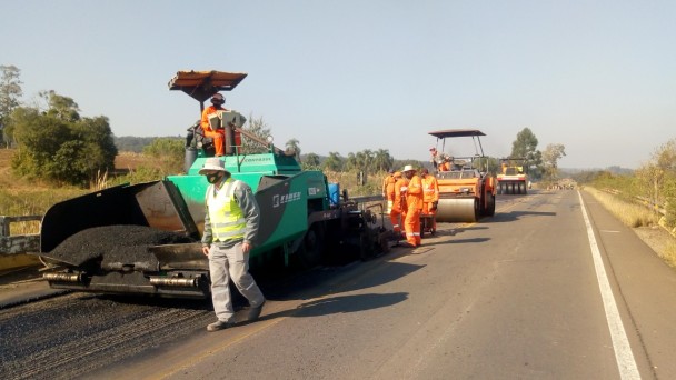A foto mostra diversos equipamentos, sendo dos rolos compressores, na rodovia.