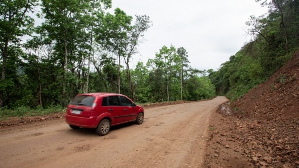 A imagem mostra um veículo trafegando por uma estrada sem pavimentação 