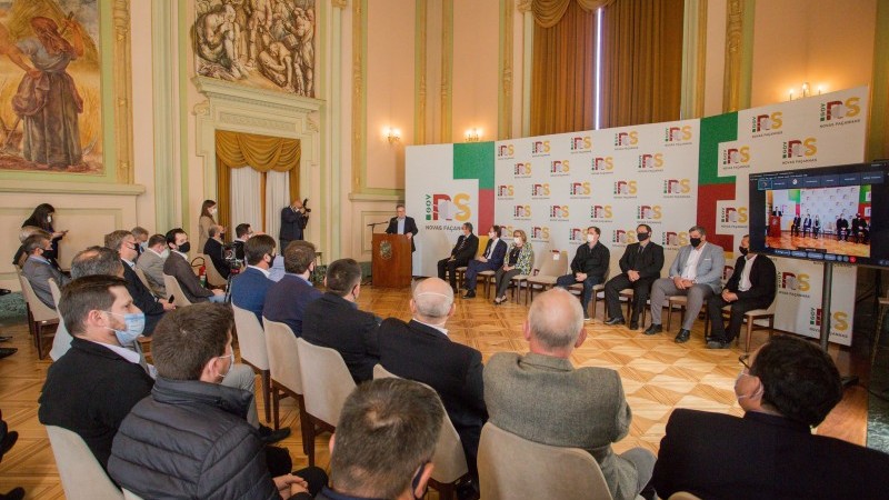 A imagem mostra o Palácio Piratini com os participantes da cerimônia.