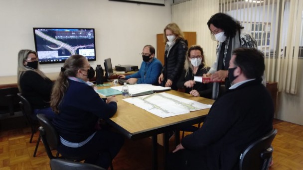 Sete pessoas reunião em volta de uma mesa analisam projetos e termos de referência para licitar serviços previstos no Plano de Obras 2021-2022.