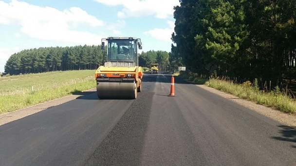 A imagem mostra máquina realizando a compactação do asfalto.