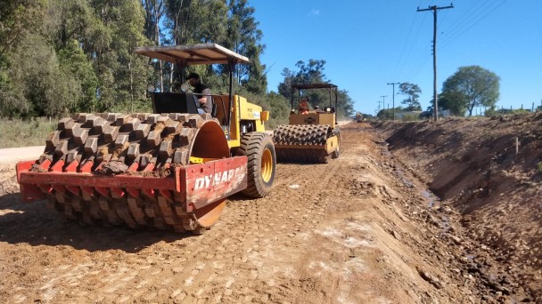 A imagem mostra as máquinas trabalhando na estrada de chão.