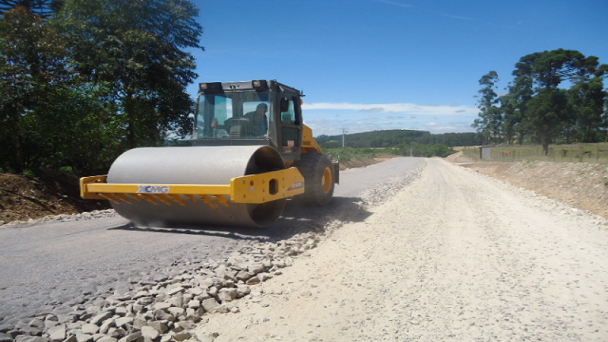 A imagem mostra a máquina realizando serviço de terraplanagem no trecho