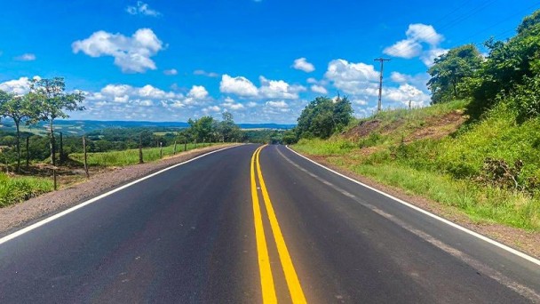Rodovia sinalizada com duplas faixas em amarelo e vegetação nas laterais.