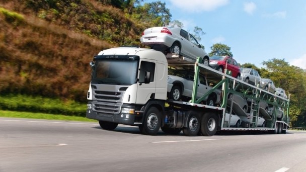 A foto mostra um caminhão-cegonha, carregado com carros, transitando em uma rodovia.