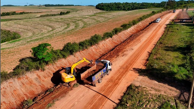 A foto aérea mostra uma retroescavadeira e um caminhão dando início às obras na ligação asfáltica a Amaral Ferrador.