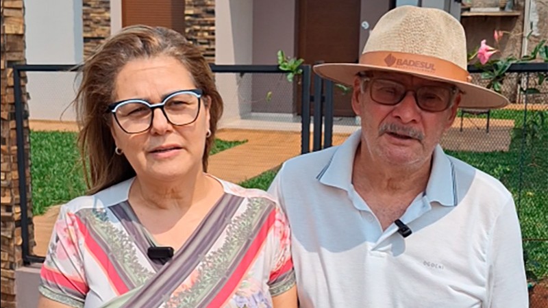 A foto mostra um casal em frente a uma casa.