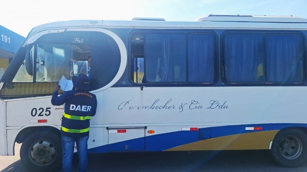 A foto mostra um fiscal do Daer vistoriando os documentos de um ônibus.